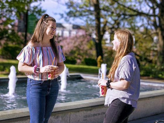 Two 学生 in conversation near fountain on campus.