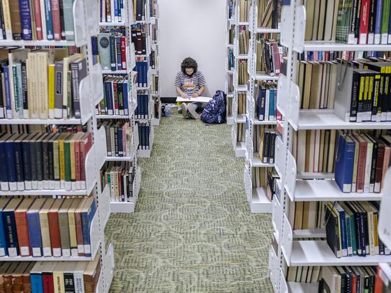 在胡佛图书馆，一名学生坐在一排排书架之间的地板上.