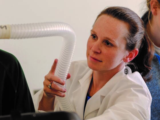 Photo of professor Jennifer McKenzie in a lab coat holding a breathing tube in the lab.