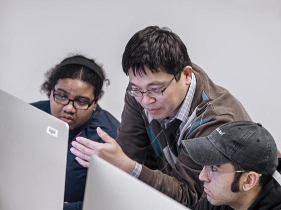 Photo of professor Paul Lin speaking with students at a computer.
