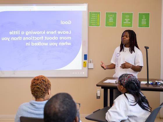 一名黑人学生在投影仪屏幕前对教室里的人讲话的照片.