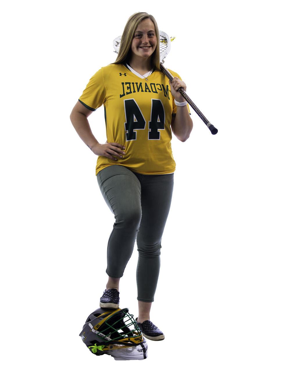 汉娜米勒 poses with a lacrosse stick over her shoulder and her foot on a helmet.
