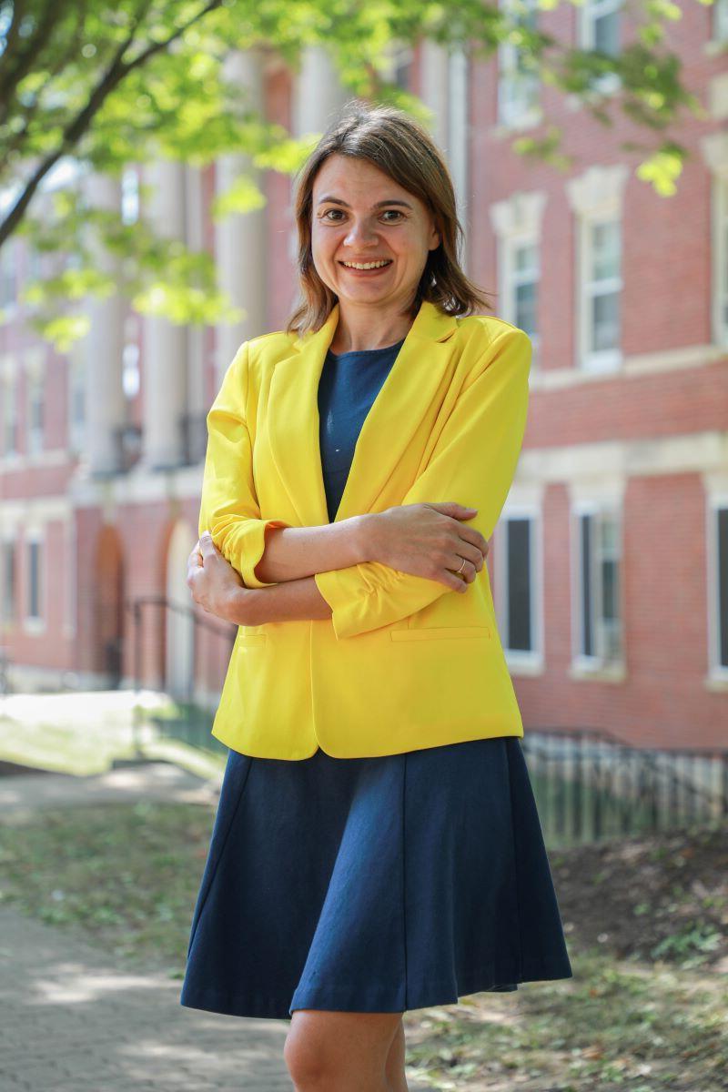 Photo of a white female in a bright yellow suit jacket standing in front of a brick academic building.