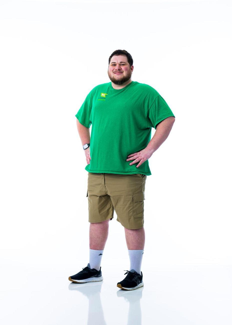 一名身穿绿色衬衫的学生双手叉腰站在白色背景前.