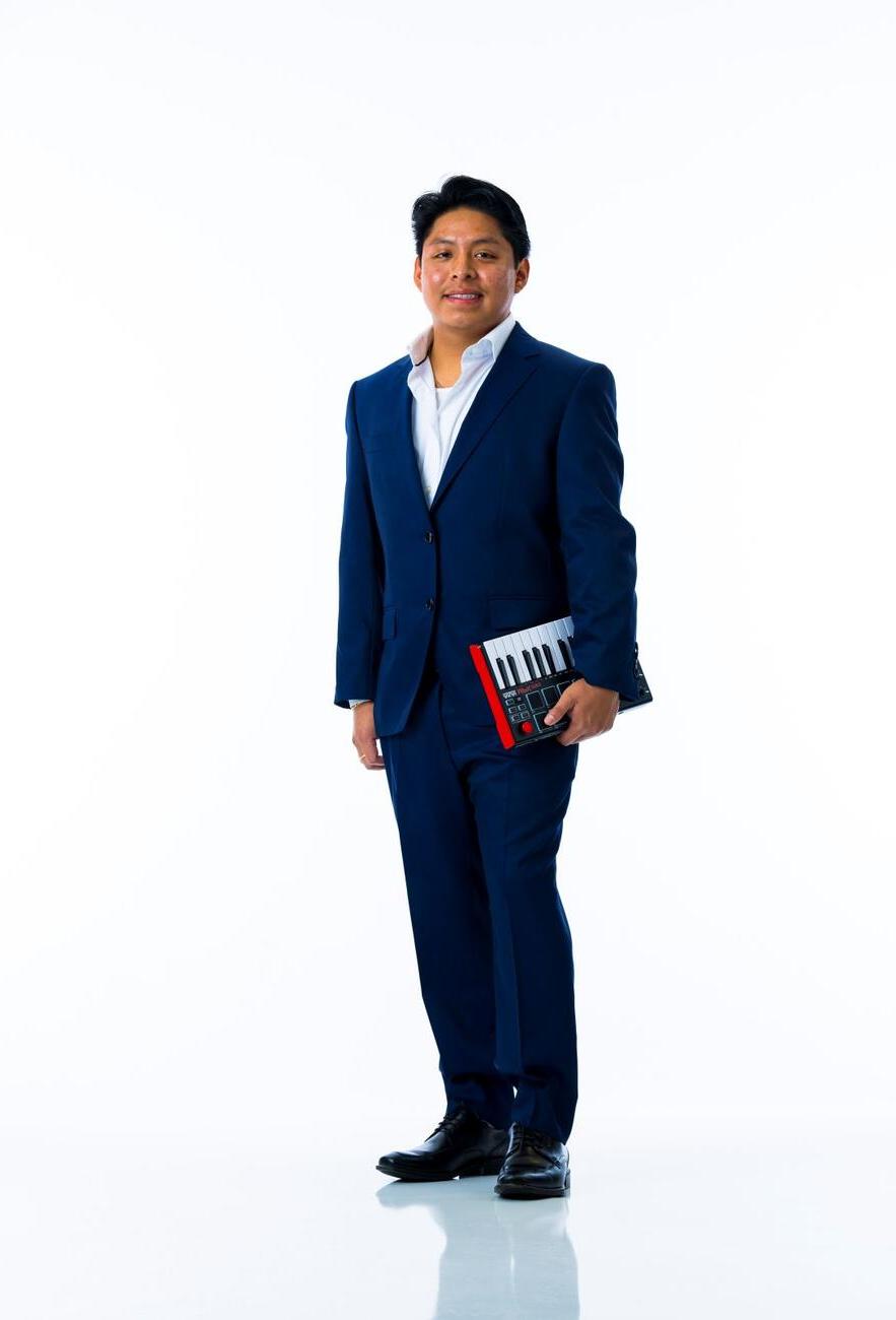 A student in a suit holds a small keyboard by their side against and white background.