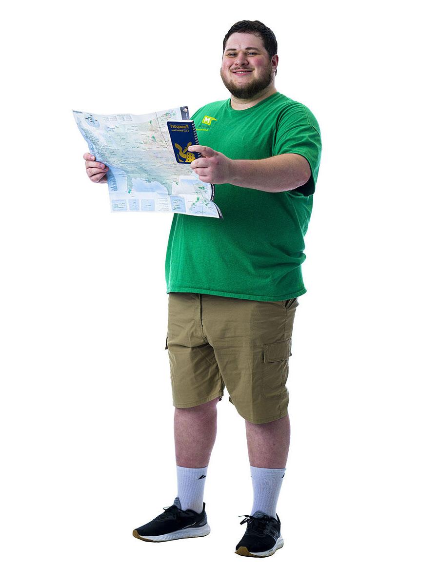A student in a green shirt stands in front of white background while holding up a map.