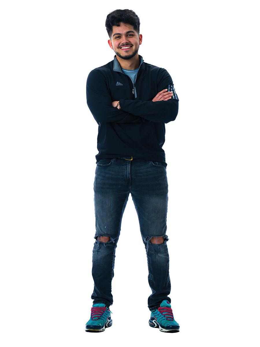 A student stands with his arms crossed in front of a white background.
