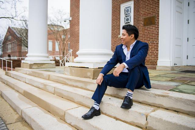 A student in a suit sits outside on steps in front of white columns.