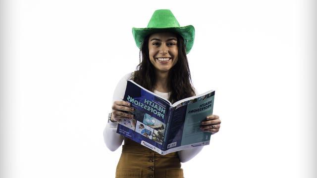 皮雷斯(Giulia Pires)戴着一顶绿色牛仔帽，手里拿着一本打开的卫生专业教科书.