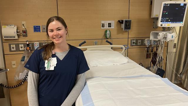 一个穿着护理服的年轻女子站在一张空病床旁.