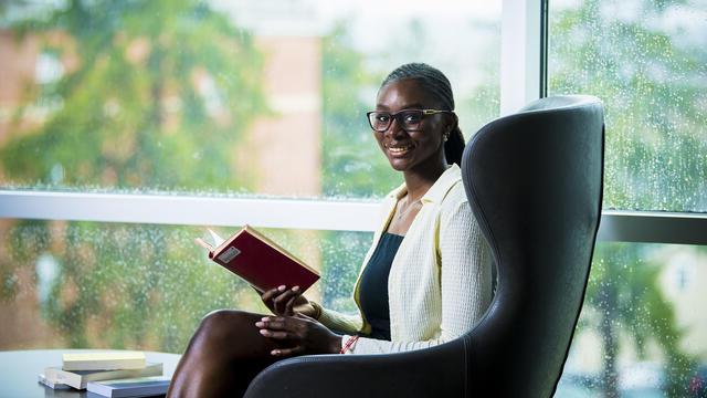 一个学生坐在窗前的椅子上，手里拿着一本书.